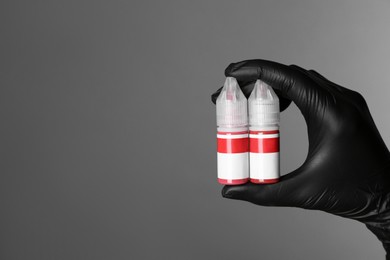 Photo of Professional cosmetologist holding bottles of pigments for permanent makeup on grey background, closeup. Space for text