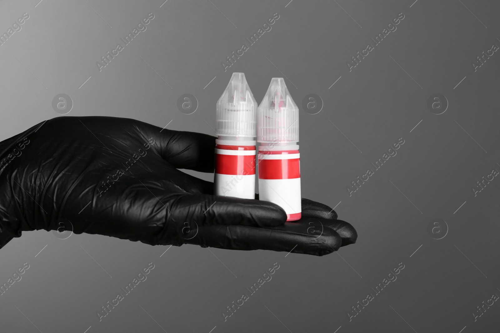 Photo of Professional cosmetologist holding bottles of pigments for permanent makeup on grey background, closeup