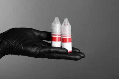 Professional cosmetologist holding bottles of pigments for permanent makeup on grey background, closeup