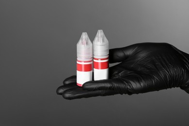 Professional cosmetologist holding bottles of pigments for permanent makeup on grey background, closeup