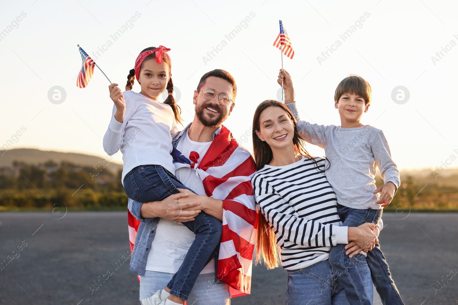 Photo of Family portrait of happy parents with children waving USA flags outdoors