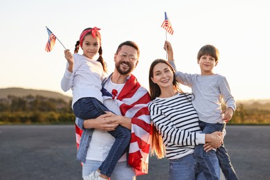 Family portrait of happy parents with children waving USA flags outdoors