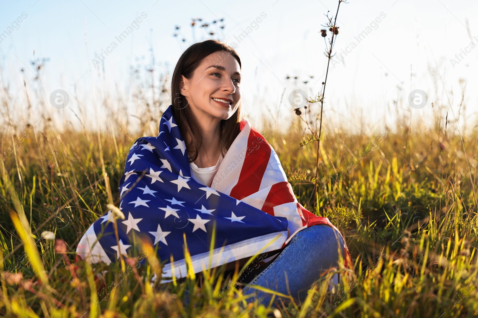 Photo of Happy woman with flag of USA sitting on grass outdoors