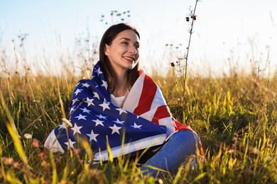 Happy woman with flag of USA sitting on grass outdoors