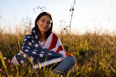 Happy woman with flag of USA sitting on grass outdoors. Space for text