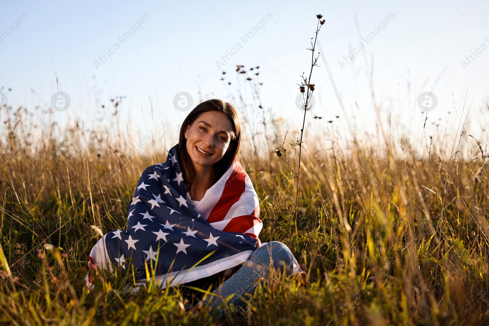 Photo of Happy woman with flag of USA sitting on grass outdoors. Space for text