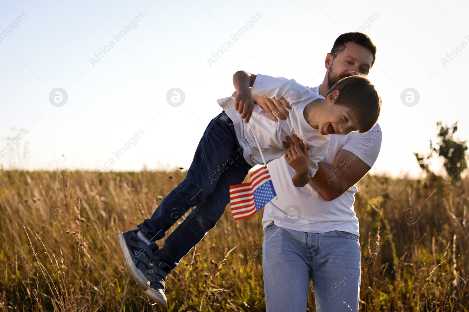 Photo of Happy father and son with flag of USA having fun outdoors. Space for text