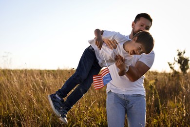 Happy father and son with flag of USA having fun outdoors. Space for text