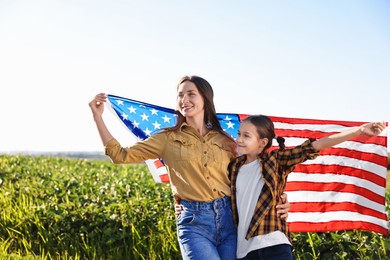 Happy mother and daughter with flag of USA outdoors. Space for text