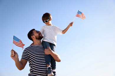 Happy father and son with flags of USA outdoors. Space for text