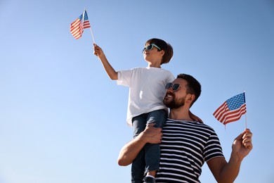 Happy father and son with flags of USA outdoors. Space for text