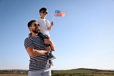 Photo of Happy father and son with flag of USA outdoors. Space for text