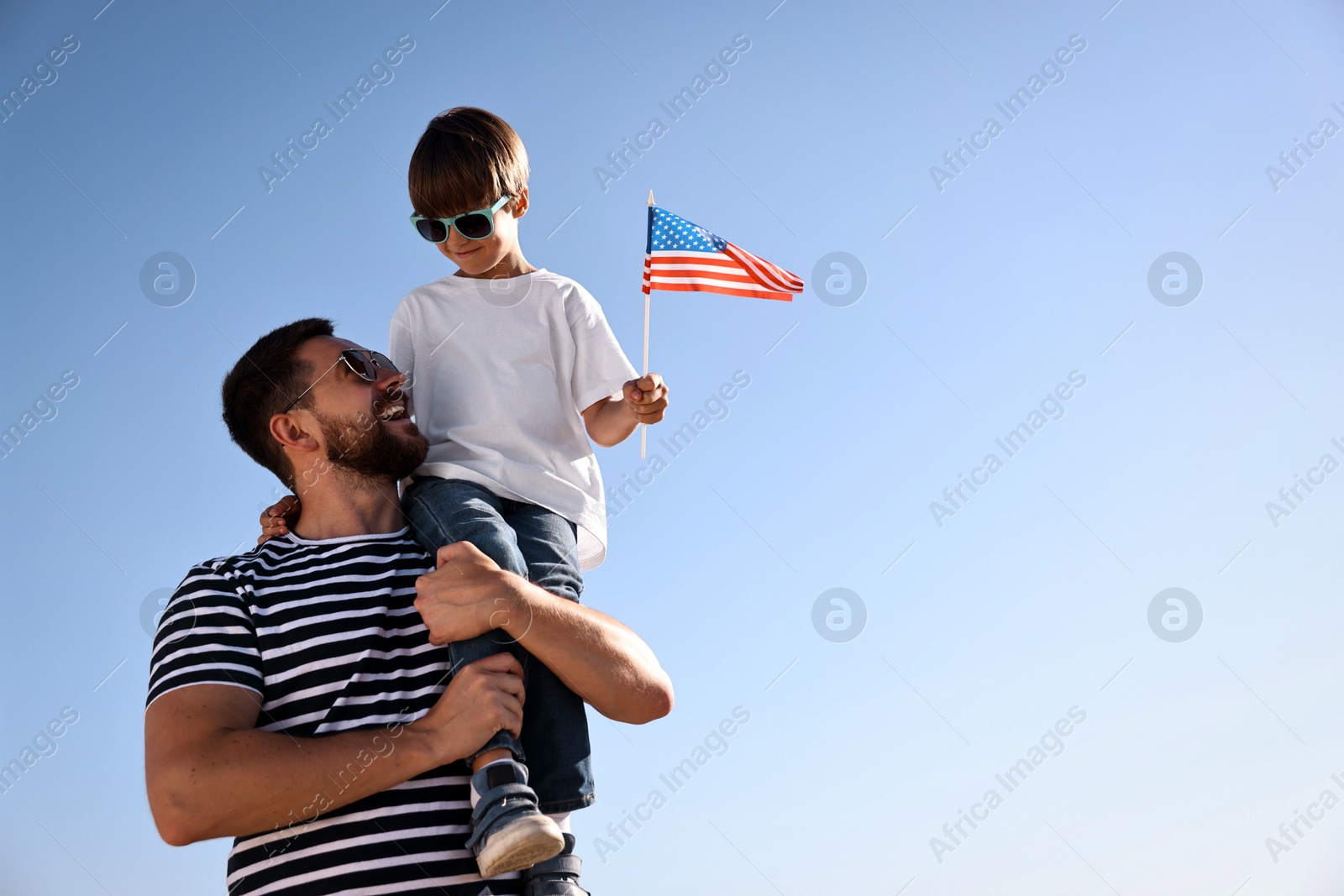 Photo of Happy father and son with flag of USA outdoors, low angle view. Space for text