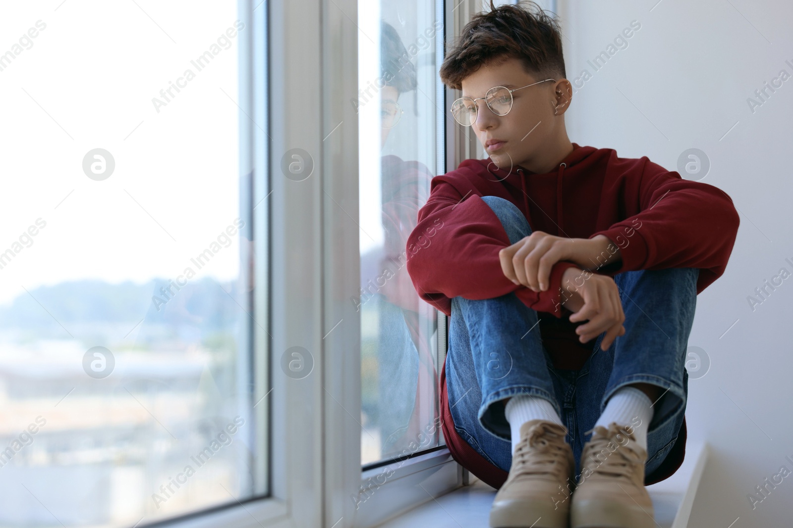 Photo of Loneliness concept. Sad teenage boy on windowsill indoors