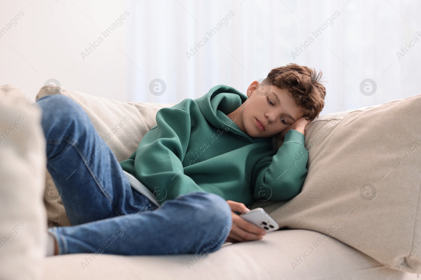 Photo of Loneliness concept. Sad teenage boy using smartphone on sofa at home