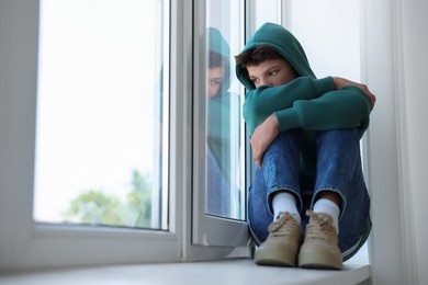 Photo of Loneliness concept. Sad teenage boy on windowsill indoors