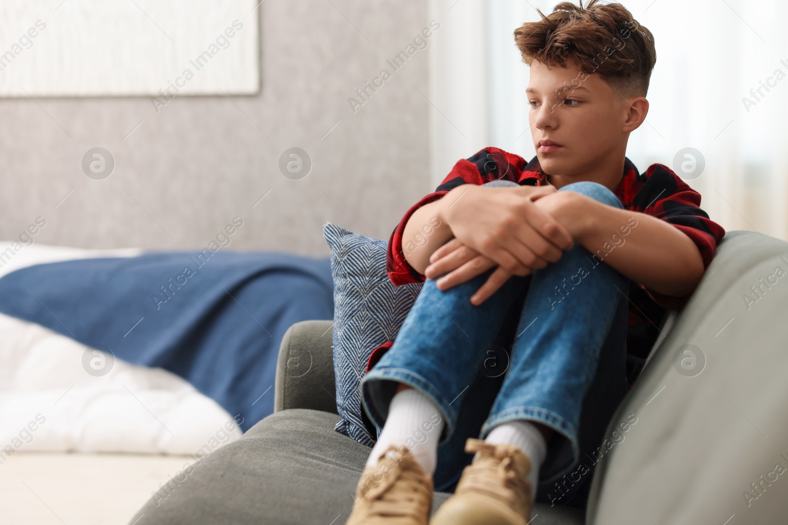 Photo of Loneliness concept. Sad teenage boy on sofa in room, space for text