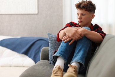 Photo of Loneliness concept. Sad teenage boy on sofa in room, space for text