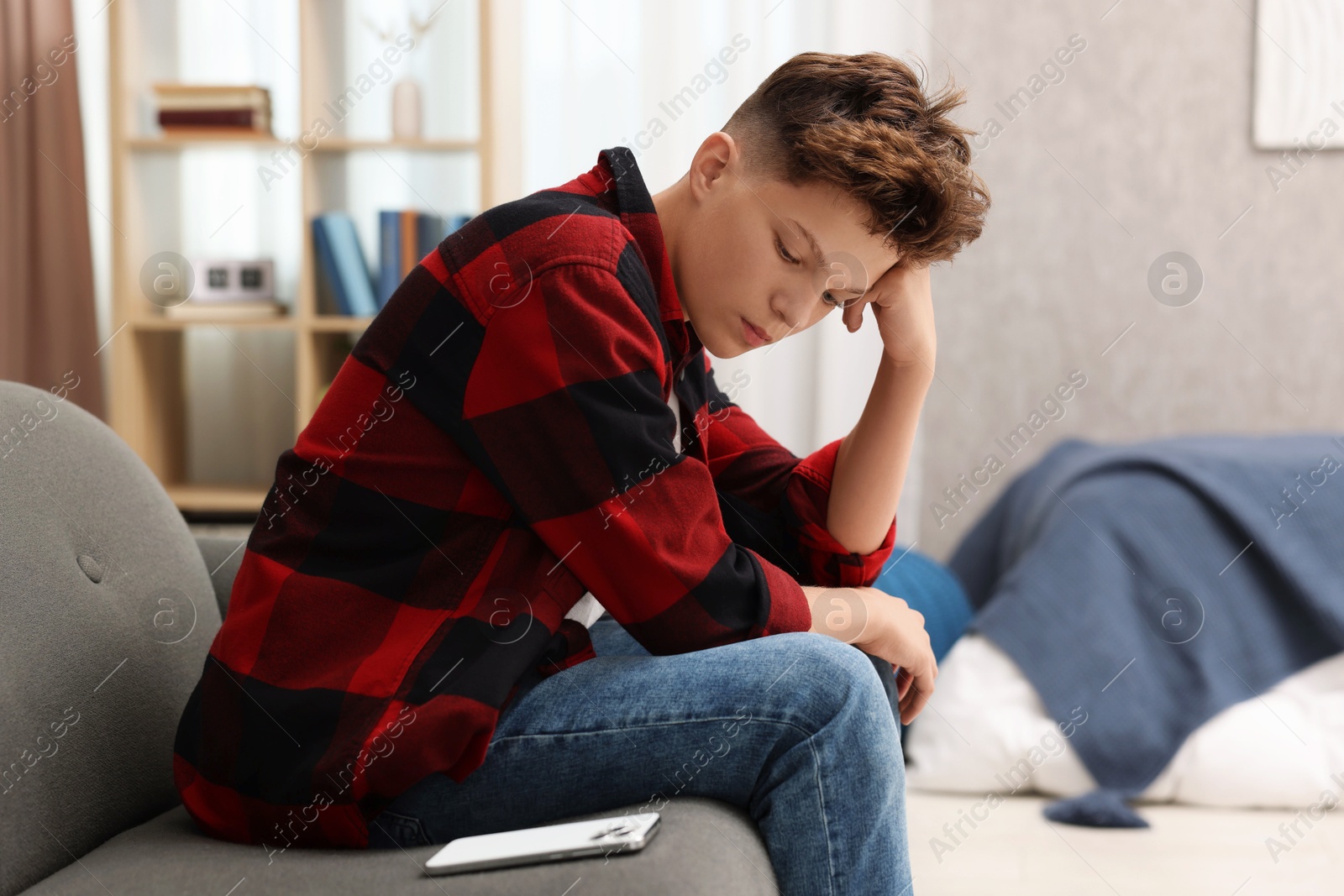 Photo of Loneliness concept. Sad teenage boy with smartphone on sofa at home