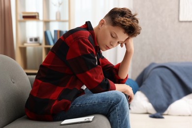 Loneliness concept. Sad teenage boy with smartphone on sofa at home