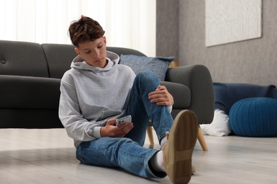 Loneliness concept. Sad teenage boy using smartphone on floor at home