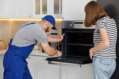 Woman looking how repairman fixing oven in kitchen