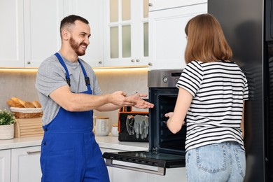 Photo of Smiling repairman consulting woman near oven in kitchen