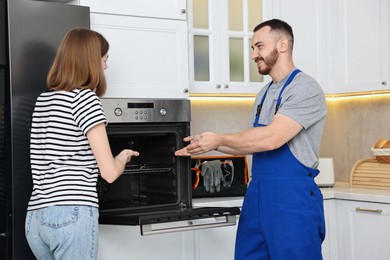 Photo of Smiling repairman consulting woman near oven in kitchen