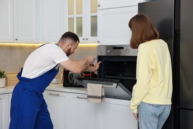 Photo of Woman looking how repairman fixing oven in kitchen