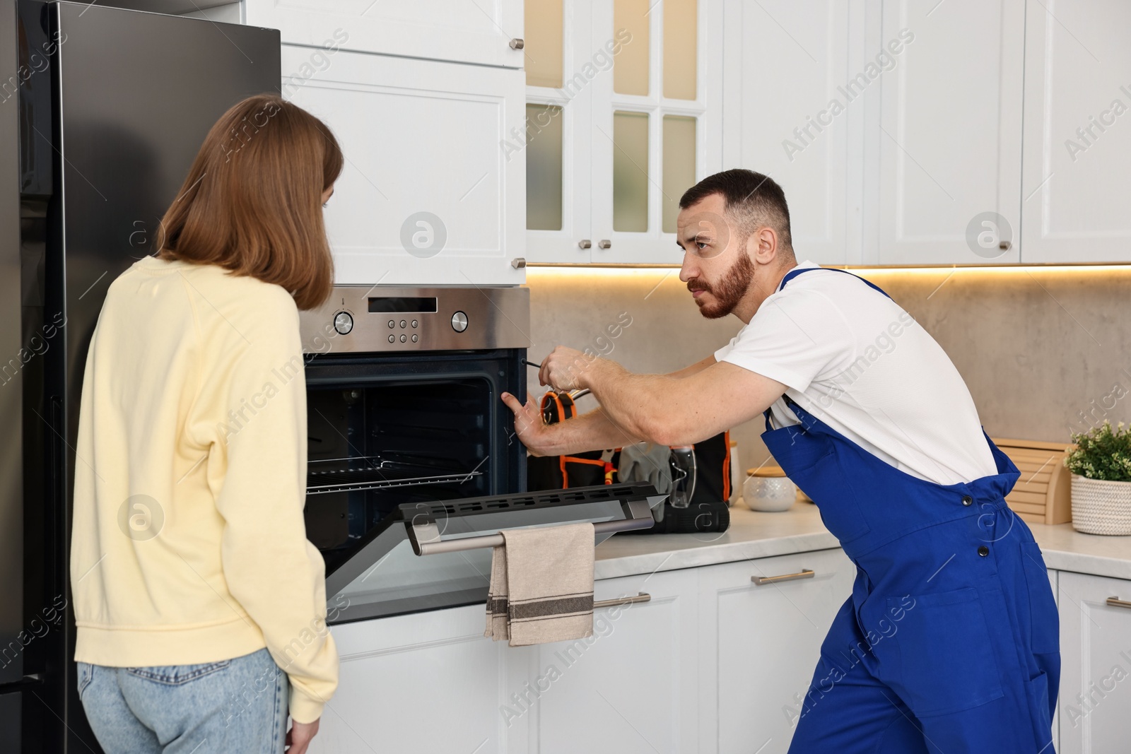 Photo of Woman looking how repairman fixing oven in kitchen