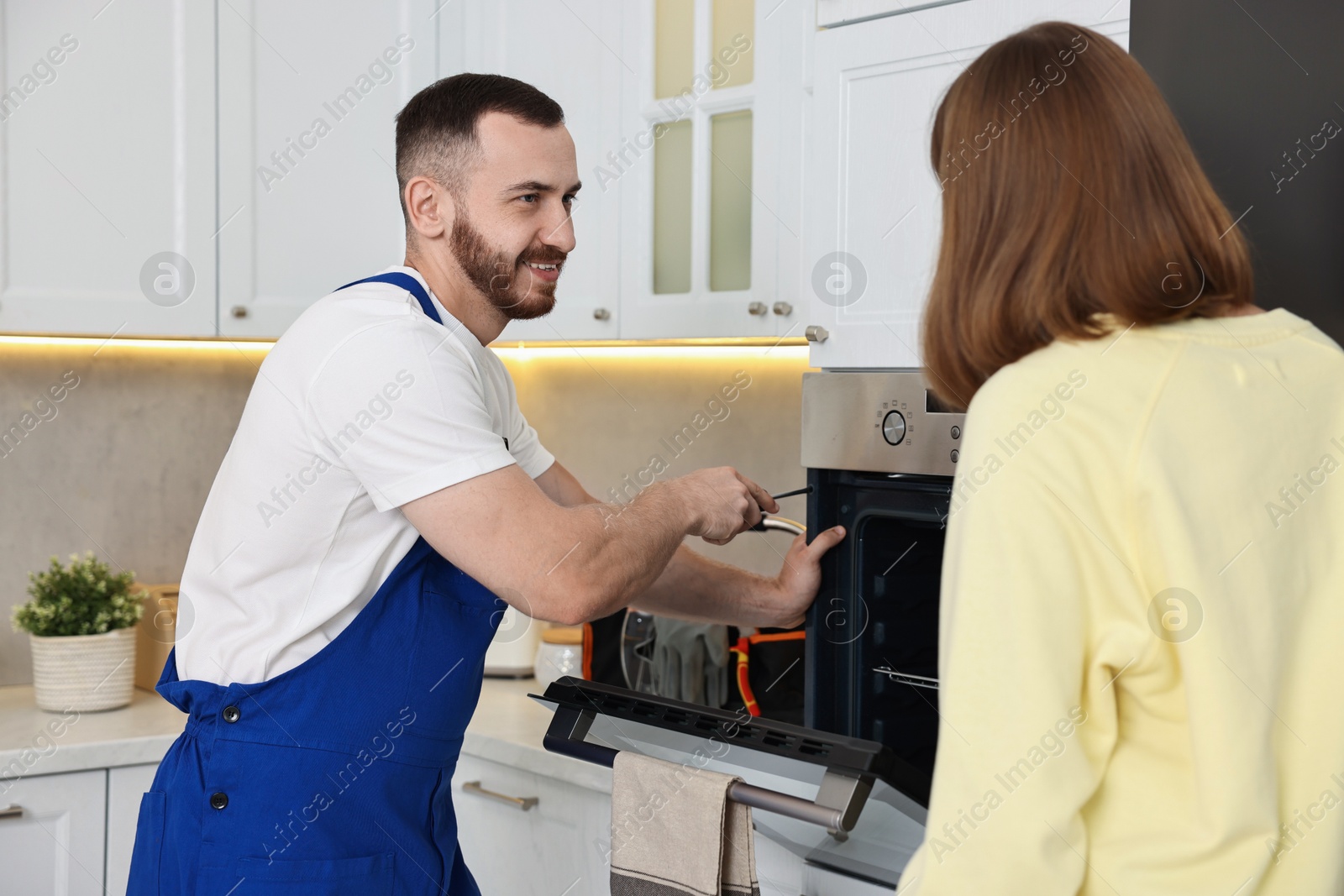 Photo of Smiling repairman consulting woman near oven in kitchen