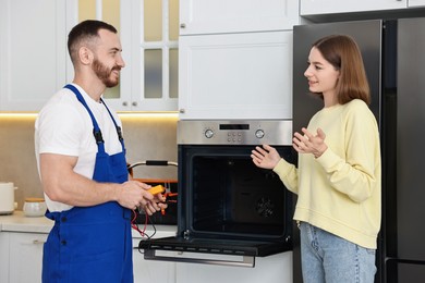 Photo of Woman talking with smiling repairman near oven in kitchen