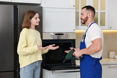 Photo of Woman talking with smiling repairman near oven in kitchen