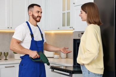 Smiling repairman with drill consulting woman near oven in kitchen