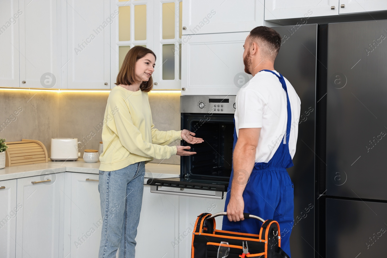 Photo of Smiling woman talking with repairman near oven in kitchen