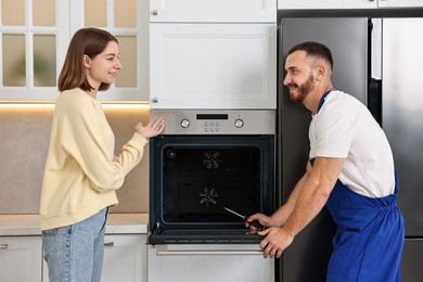 Woman talking with smiling repairman near oven in kitchen