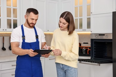 Woman and repairman signing documents near oven in kitchen