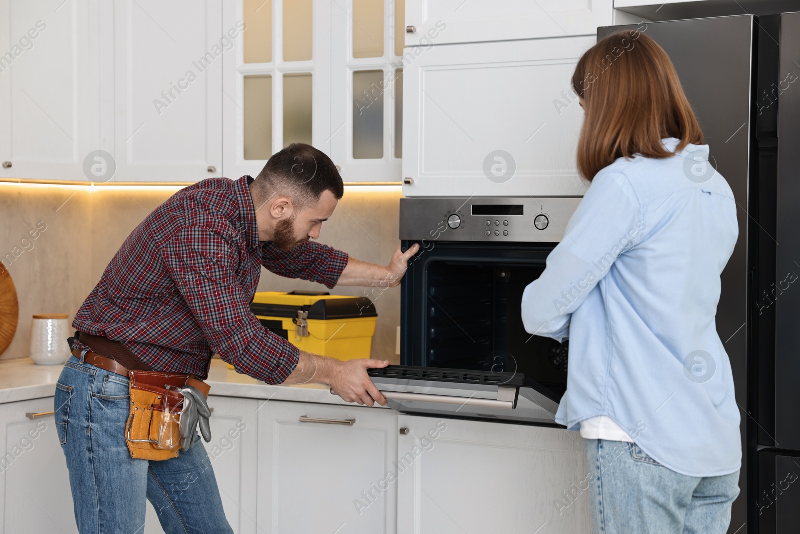 Photo of Woman looking how repairman examining oven in kitchen