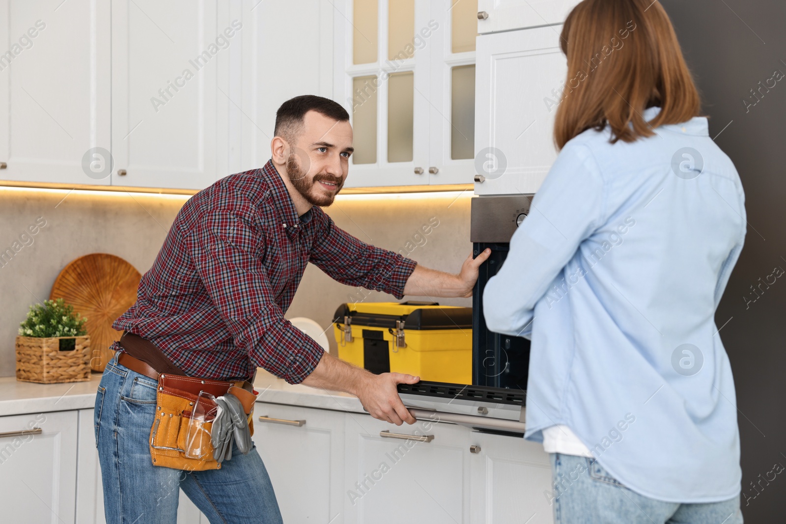 Photo of Smiling repairman consulting woman near oven in kitchen