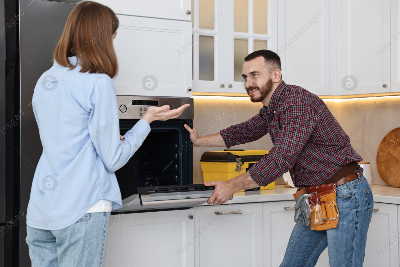 Photo of Smiling repairman consulting woman near oven in kitchen