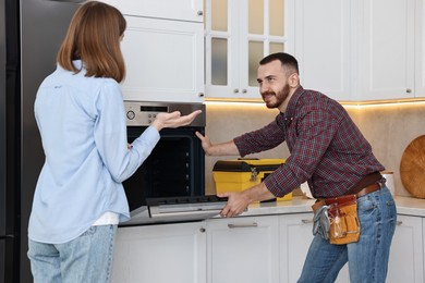 Smiling repairman consulting woman near oven in kitchen