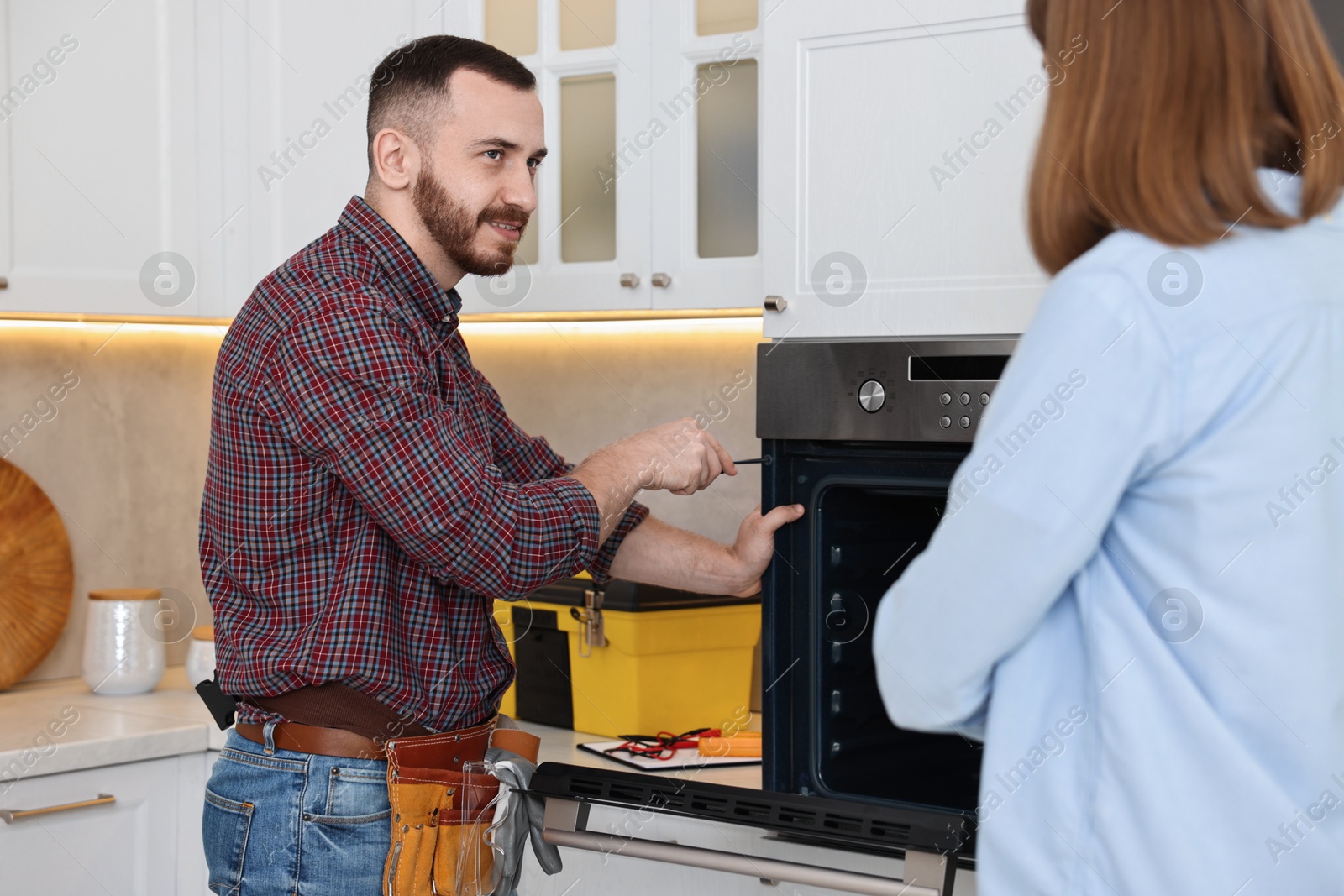 Photo of Smiling repairman fixing oven near woman in kitchen