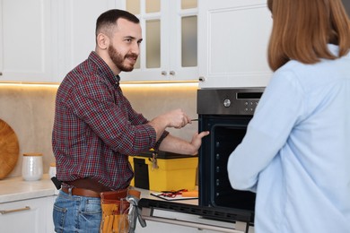 Smiling repairman fixing oven near woman in kitchen