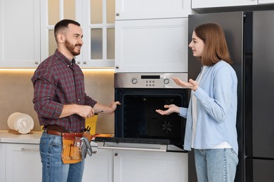 Smiling repairman consulting woman near oven in kitchen