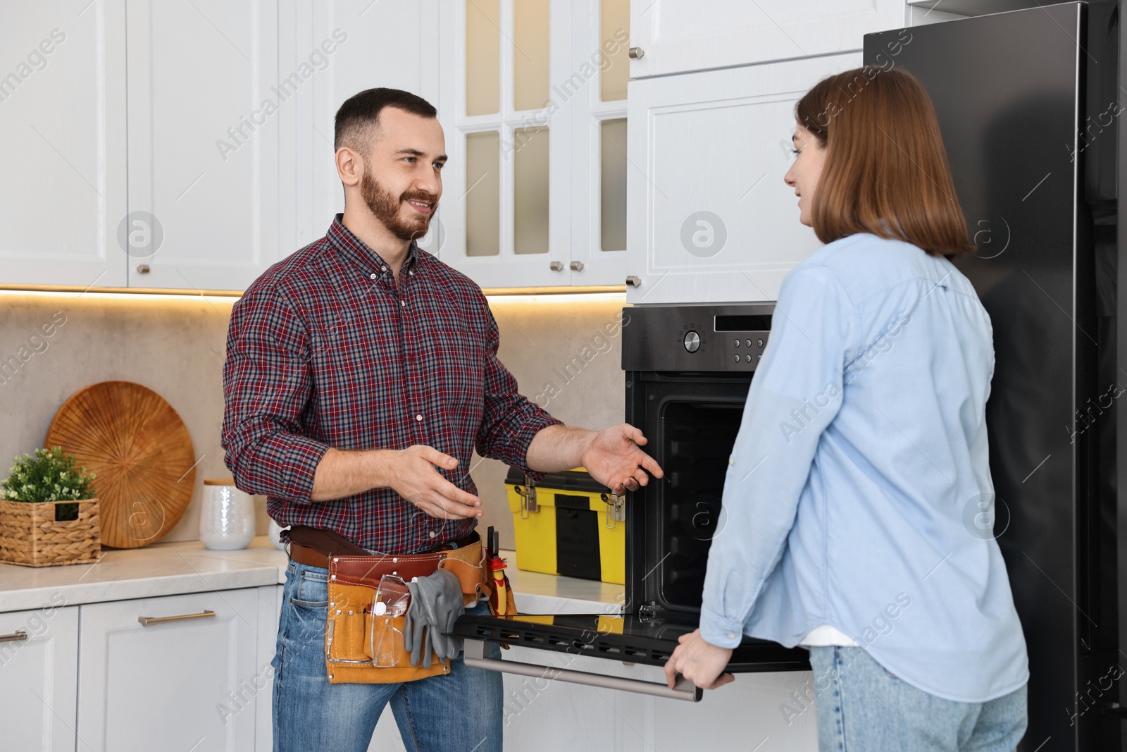 Photo of Smiling repairman consulting woman near oven in kitchen