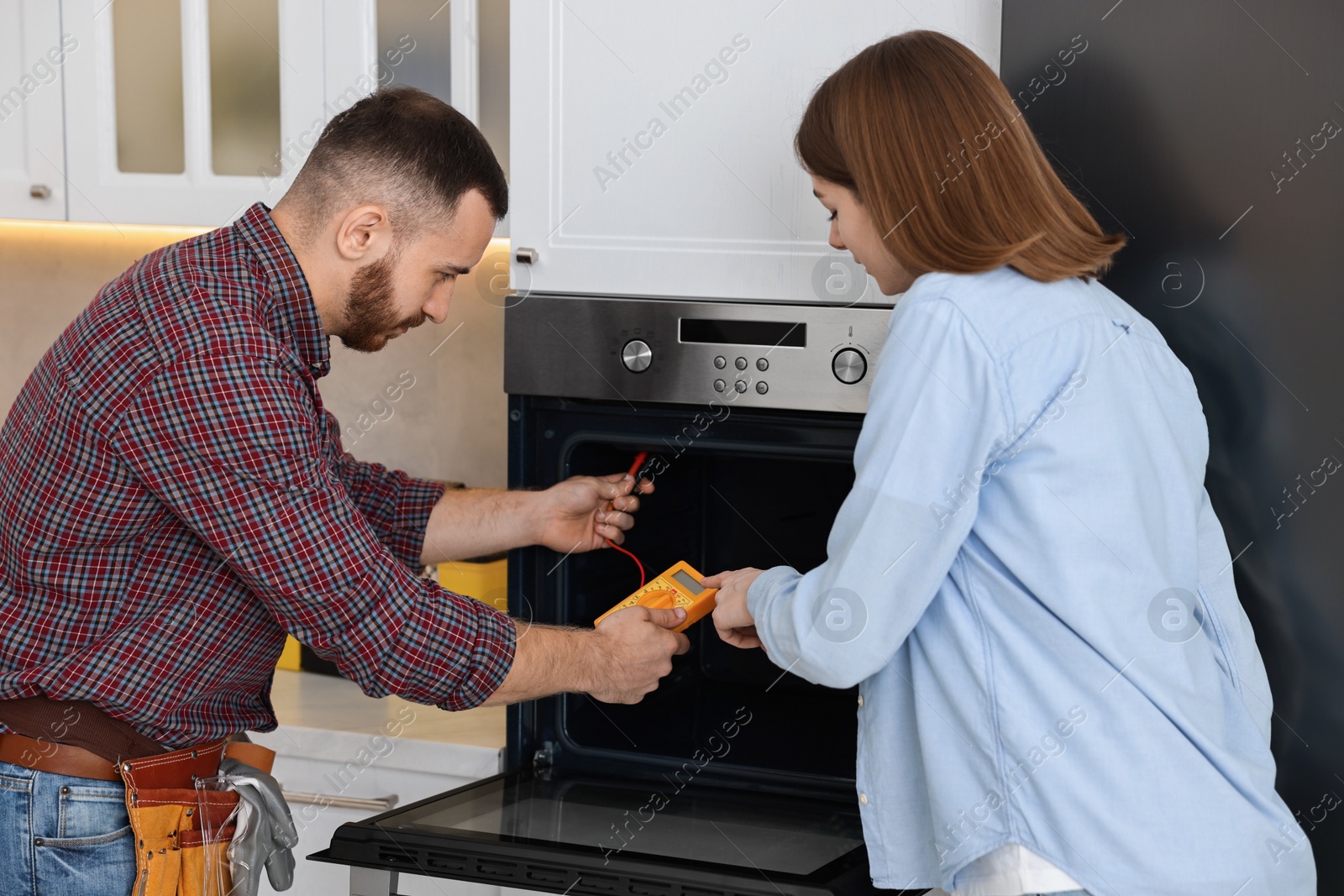 Photo of Repairman showing woman how to use multimeter near oven in kitchen