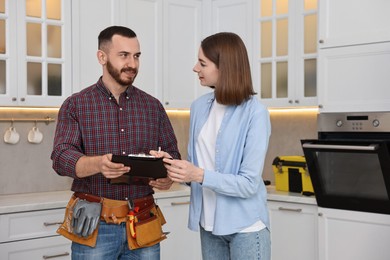 Woman and repairman signing documents near oven in kitchen