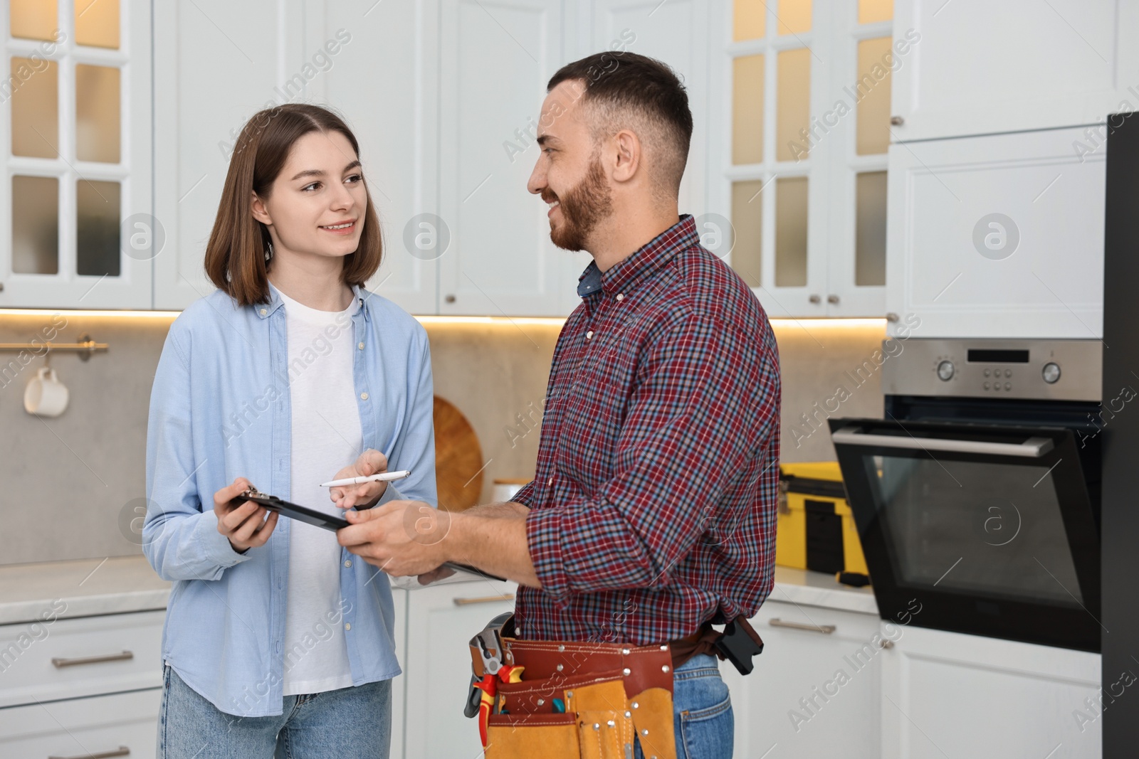 Photo of Smiling woman and repairman signing documents near oven in kitchen