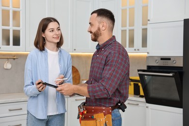 Photo of Smiling woman and repairman signing documents near oven in kitchen