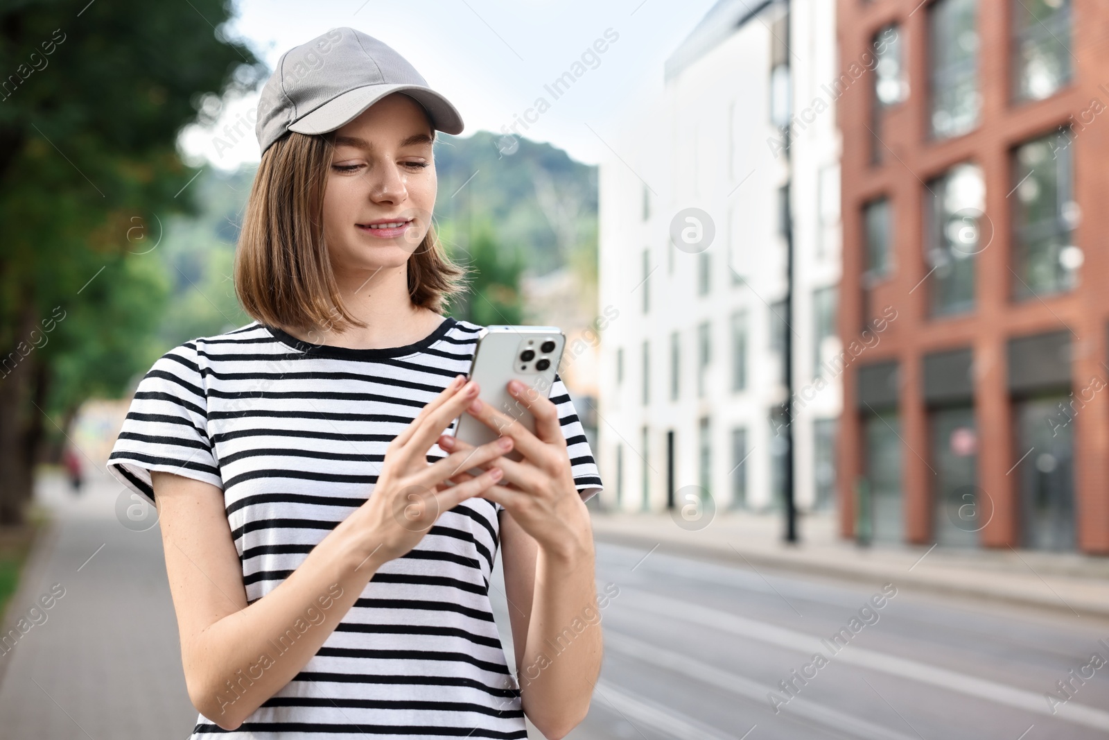 Photo of Portrait of smiling woman in baseball cap with smartphone outdoors. Space for text